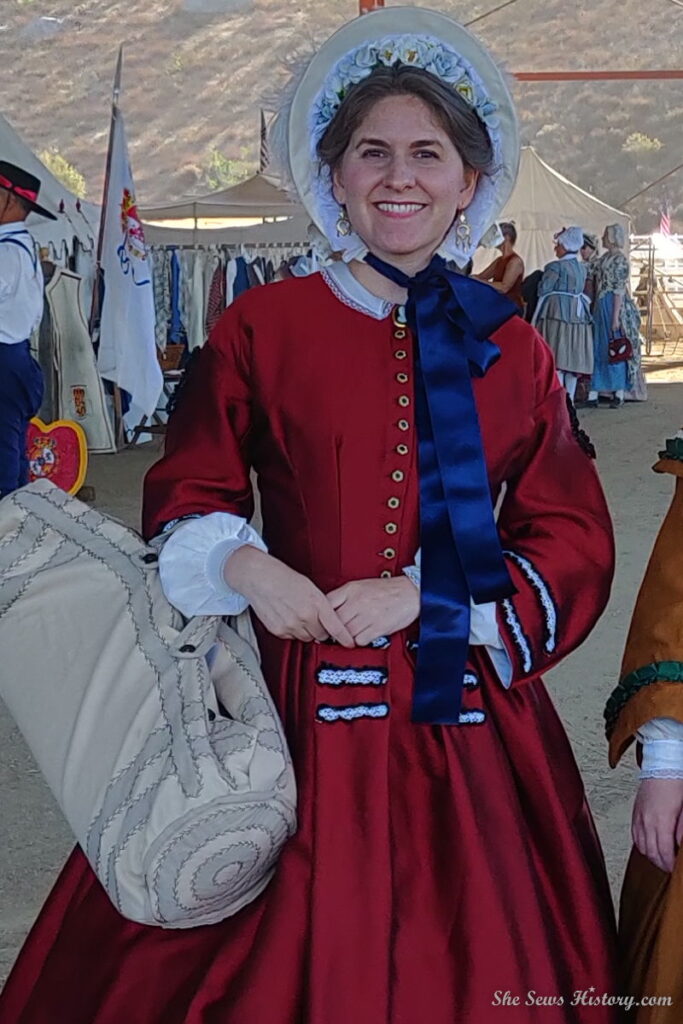 Reenactor portraying Julia Grant Mrs. Ulysses Grant in red silk reproduction dress and 1860s traveling bag
