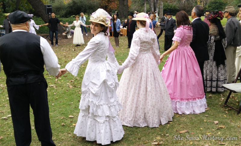 Girl in 1870's bustle dress doing English Country dance with friends in a circle