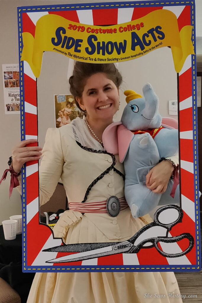 18th century ensemble with a dumbo stuffed disney charachter and a Costume College 2019 sign